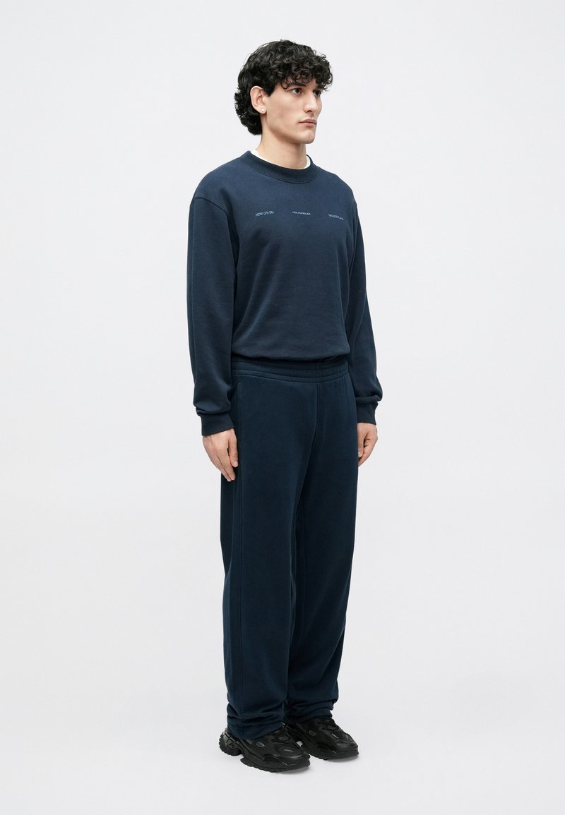 Survêtement bleu marine en tissu doux ; comprend un sweat-shirt à col rond avec des accents de logo et un pantalon à coupe décontractée avec une ceinture élastique.