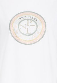 Tissu blanc avec un logo circulaire étincelant en strass comportant les lettres "PULZ JEANS" et les lettres stylisées "P", "J", "L" au centre.