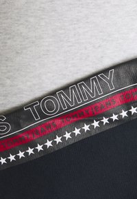 Gros plan sur un tissu avec le texte "Tommy Jeans", des étoiles blanches et des bandes de couleur noire, rouge et grise sur un vêtement.