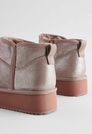Bottines roses avec une finition pailletée, doublure douce, tirant, et une semelle robuste légèrement surélevée. Surface texturée et bords lisses.