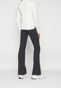 Vit långärmad topp med sidoflikar, kombinerad med svarta utsvängda byxor. Outfiten kompletteras av silver- och blå sportskor.