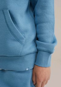 Felpa azzurra realizzata in tessuto morbido, con tasca a marsupio, polsini a costine e un piccolo cartellino con logo sull'orlo.