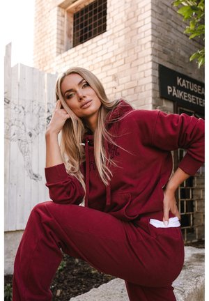 Pealt veini punane kapuutsiga dressipluus ja dressipüksid, valmistatud pehmest kangast, millel on paelaga reguleeritav nöör ja tasku detailid. Komplekt on lõdva lõikega ja lihtsa disainiga.