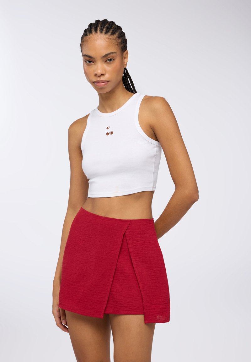 Top corto bianco con scollo rotondo e dettagli ritagliati, abbinato a una mini gonna rossa testurizzata con design a incrocio.