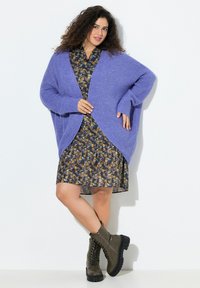 Lavendel överdimensionerad stickad kofta över en mönstrad klänning i mörka färger, kombinerad med olivgröna snörstövlar och en texturerad tyg.