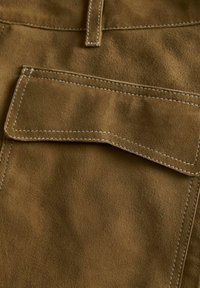 Tissu en daim marron avec une texture lisse ; présente une poche cousue avec un rabat plat et une couture beige contrastante sur les bords.