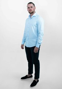  Lichtblauw overhemd met lange mouwen, gecombineerd met donkere broeken en zwarte instapschoenen. Glad textuur, getailleerd ontwerp.