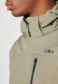 Oliven grøn softshell jakke med høj krave, lynlåslommer og broderet logo. Glat stof med mat finish.