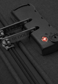 Primer plano de una bolsa de viaje negra con cremalleras dobles, con la marca "REDOLZ", un mecanismo de bloqueo y una superficie de nailon texturizada.