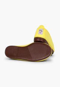Gele canvas instap schoenen met een bruine rubberen zool, voorzien van een label met een cartoonfiguur en "Made in Spain" op de hiel.