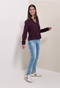 Blouse à manches longues violet foncé associée à un jean slim bleu clair et des baskets blanches avec des accents bordeaux et des détails verts.