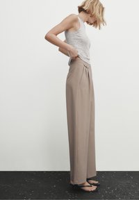 Débardeur gris clair et pantalon taille haute beige avec plis. Le tissu semble lisse avec un design fluide. Sandales plates simples.