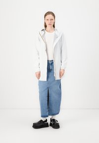 Bela lahka jakna z kapuco in zadrgo, v kombinaciji z jeans krilom z razporkom spredaj in črnimi platform sandali.