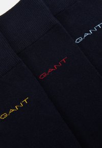 Tres pares de calcetines navy con el logo "GANT" en bordado amarillo, rojo y azul claro en el puño. Textura suave y diseño acanalado.