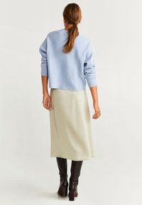 Suéter azul claro con hombros caídos, combinado con una falda midi crema y botas altas marrón oscuro. Texturas suaves y diseño sencillo.