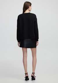Sweatshirt noir à manches longues, avec un col rond et une coupe décontractée, associé à une mini-jupe en cuir noir et des talons hauts à lanières.