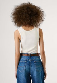 Canottiera bianca a coste con scollatura rotonda, abbinata a jeans blu in denim a vita alta e una cintura marrone.