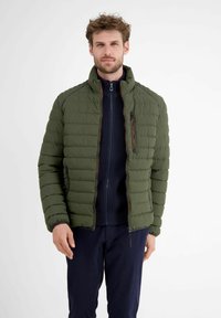 Puffermantel in Dunkelgrün, mit hohem Kragen, gestepptem Muster, seitlichen Taschen und einer Brusttasche mit Reißverschluss und kontrastierender Naht.