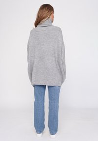 Szary, oversize sweter z golfem o prążkowanej fakturze, w połączeniu z niebieskimi jeansami prostymi i białymi sneakersami, widok z tyłu.