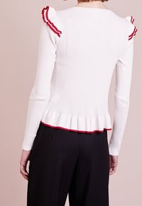 Weißes, geripptes Langarmoberteil mit roten Rüschendetails an den Schultern und am Saum, im Peplum-Design.