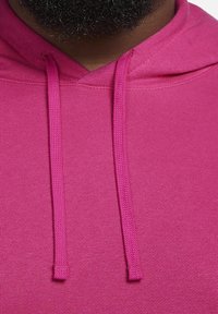 Fuchsiová mikina s kapucí z měkkého materiálu, vybavená stahovací šňůrkou na kapuci a bezšvovým designem. Barva je výrazná a jednotná bez vzorů.