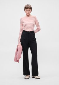 Blusa de manga longa às riscas rosa e branca, calças pretas de cintura alta, cinto preto, sweater de malha rosa e sapatos planos de cor clara.