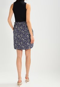 Blå kjol med paisleymönster, elastisk midja, knälängd, tillverkad av lättviktsmaterial. Bärs med en svart ärmlös topp och beiga klackar.