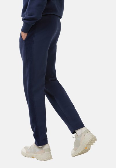 Navyblauwe joggingsbroeken van zachte fleece, met zijzakken, taps toelopende benen en elastische boorden, gecombineerd met lichtgekleurde sneakers.