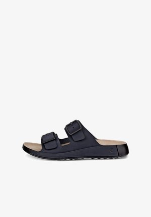 Czarna klapka na płaskiej podeszwie z dwoma regulowanymi paskami zapinanymi na klamry oraz beżową wyściółką pod stopą, widziana z zewnątrz.