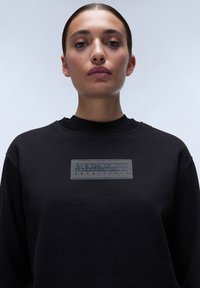 Felpa nera con scollatura rotonda, dotata di un'etichetta logo grigia testurizzata. Il tessuto liscio e il taglio rilassato mettono in evidenza un design contemporaneo.