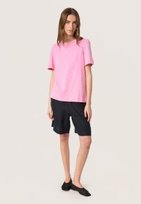 Lyserød bomulds t-shirt med korte ærmer, parret med mørke linned shorts og sorte flade sko. Enkel, afslappet pasform og afslappet design.