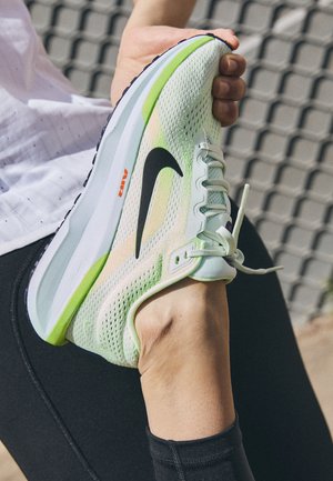 Hellgrüner Nike-Laufschuh mit Mesh-Obermaterial, schwarzem Swoosh und orangefarbenem 'AIR'-Logo. Designed für Komfort, mit einer strukturierten Sohle.