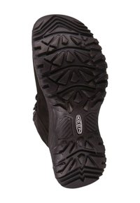 Sort gummistøvlesål med dybe slidmønstre, der har trekantede og rektangulære knotter for greb; indeholder en logo på hælen.
