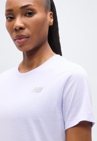 Μωβ λιλά κοντομάνικο T-shirt από απαλό ύφασμα, με διακριτικό ασημί λογότυπο New Balance στο αριστερό μέρος του στήθους.