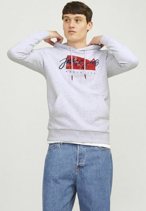 Grauer Hoodie mit einem Front-Graphic in Rot und Schwarz, verstellbaren Kordeln und einer Kängurutasche. Getragen mit blauen Jeans.