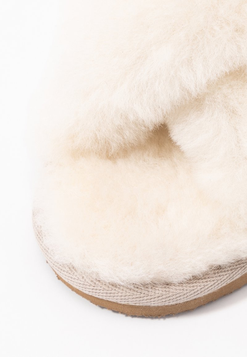 Pluizige witte schapenvacht bovenkant met een zachte textuur, gebogen vorm en lichtbeige stoffen accenten, bovenop een lichtbruine rubberen zool.