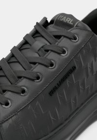 Gros plan d'une sneaker noire Karl Lagerfeld avec des motifs d'étoiles en relief, des lacets noirs et un logo sur le côté et la languette.