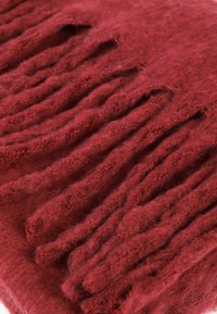 Rød frynsed tekstil med en blød, struktureret overflade og lag af tråde. Det overordnede udseende er rigt og varmt.