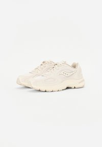 Baskets de sport beige en mesh et cuir, avec un design courbé, des panneaux texturés et une semelle en caoutchouc avec un motif de traction visible.