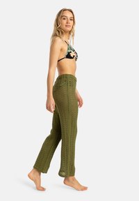 Crocheted olive green pants with a loose fit and textured pattern, featuring an elastic waistband and open-knit design.