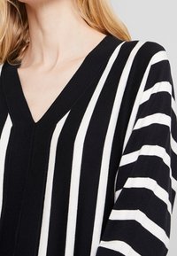 Striped pullover sweater featuring a deep V-neck, black and white fabric, and long sleeves with alternating thick and thin stripes.