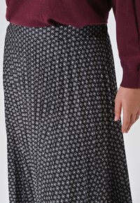 Schwarzer Faltenrock mit einem gemusterten Design aus kleinen weißen Quadraten. Der Bund ist einfarbig schwarz und hat eine glatte Textur.