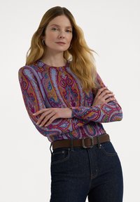 Hosszú ujjú, színes paisley mintás pulóver, puha anyagból készült, sötétkék farmernadrággal és ezüstcsatos barna övvel párosítva.