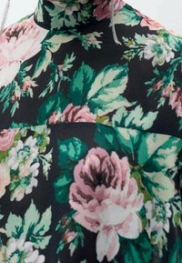 Tissu à motif floral avec un fond sombre, présentant des fleurs roses et vertes. Design à col haut avec une texture douce et lisse.