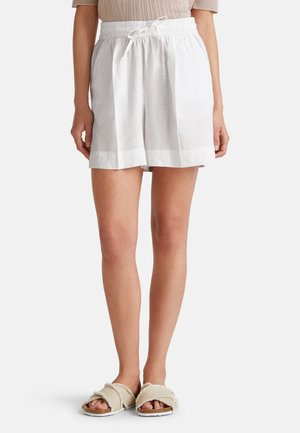 Shorts en lin blanc avec une taille élastique et un cordon de serrage. Présentent une coupe ample et un ourlet à revers. Associés à des sandales à glissière beiges.