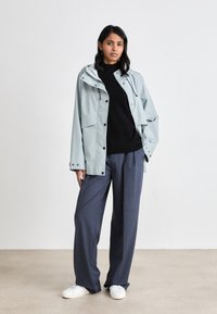 Light blue rain jacket with a hood, front pockets, and snap closures, paired with a black sweater and loose gray trousers. White sneakers.