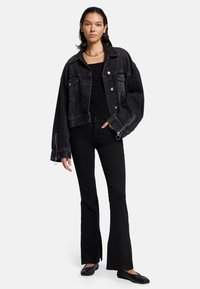 Zwarte denimjack met oversized mouwen en opgestikte zakken, gedragen over een zwarte top en gecombineerd met flared zwarte broeken en zwarte flats.