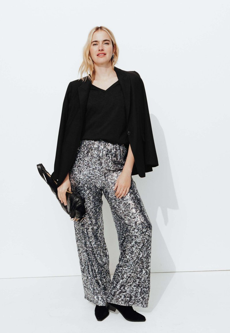 Blazer noir sur un haut noir, associé à un pantalon large en sequins argentés. Les accessoires comprennent un sac à main noir et des bottes pointues noires.