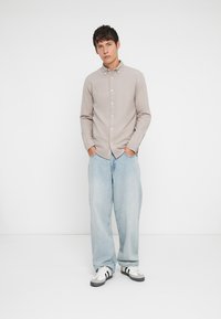 Svetlo béžová košeľa na gombíky s golierom, skombinovaná so voľnými svetlomodrými džínsami a čierno-bielymi teniskami; minimalistický dizajn.