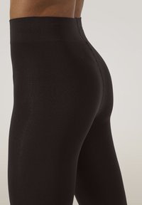 Svarte højtaljede leggings lavet af glat, strækbart materiale. Har et sømløst design og en blød, figursyet tekstur.